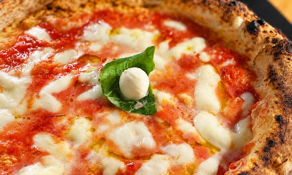 Primo piano di una pizza con pomodoro, mozzarella, basilico e cornicione alto e dorato.