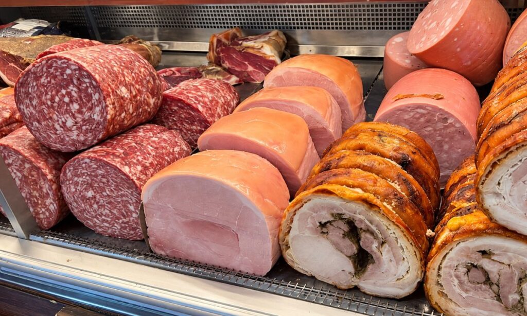 Banco refrigerato con salami, prosciutto cotto, mortadella e porchetta esposti dietro il vetro