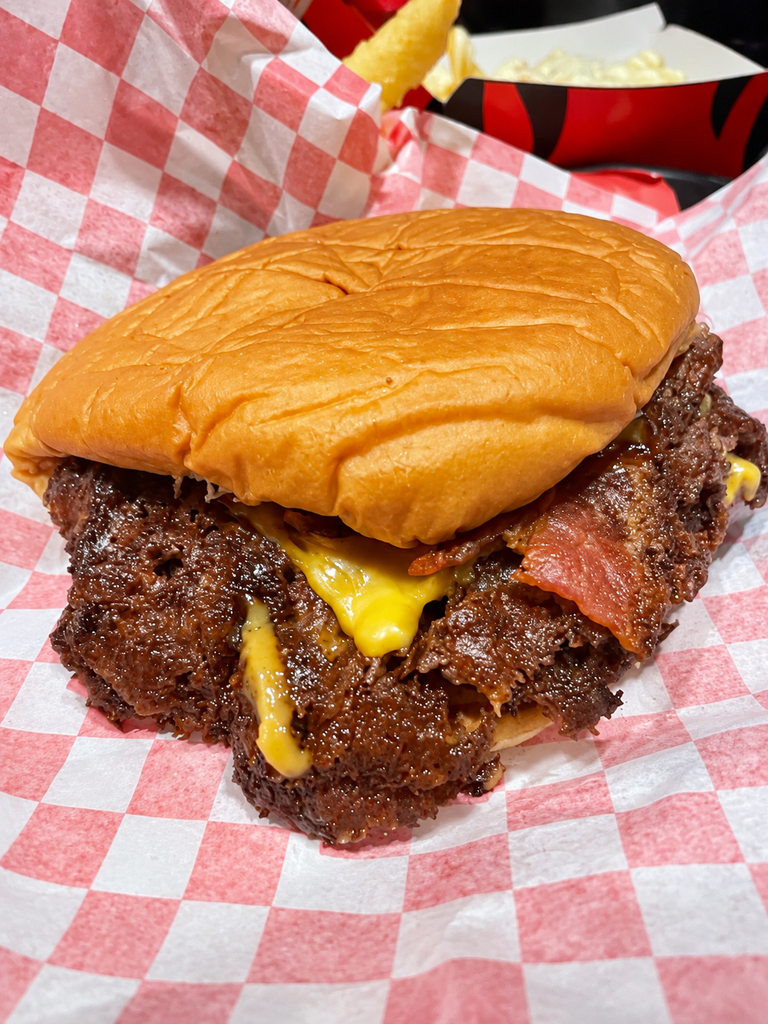 Smoke Burger su carta a scacchi rossi e bianchi, con doppio patty, formaggio fuso e bacon.