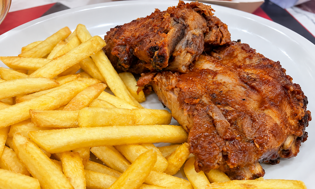Costine di maiale dorate accompagnate da patatine fritte su un piatto bianco.