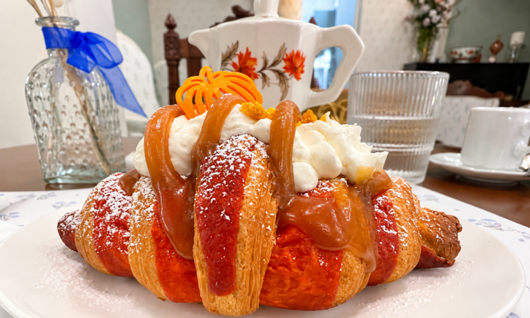 Croissant Pumpkin Spice con panna e caramello salato, con una Moka a motivi floreali sullo sfondo.