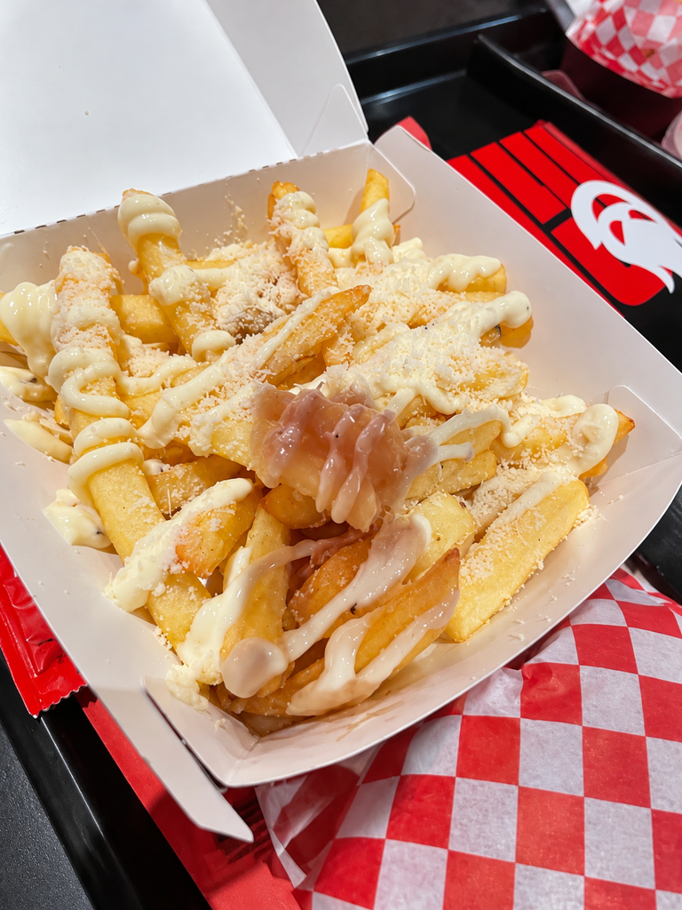 Patatine in una vaschetta aperta, condite con salsa chiara e formaggio grattugiato.