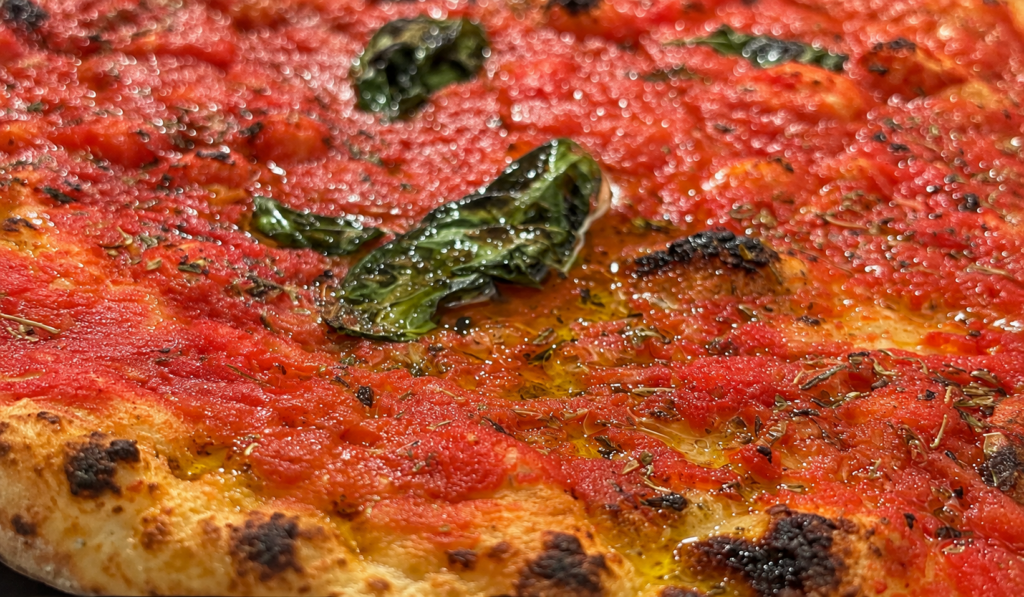 Primo piano della pizza marinara di Da Michele a Cosenza, con pomodoro, foglie di basilico, origano e bordo dorato con segni di cottura.