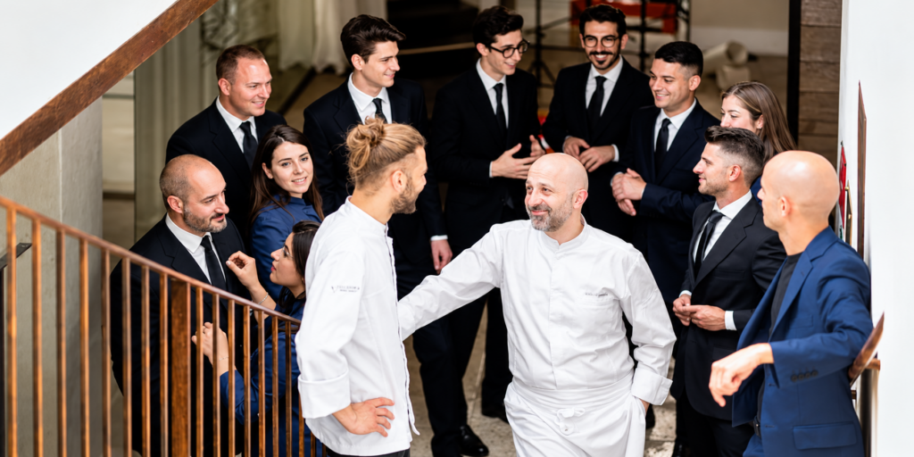 La squadra del Reale riunita su una scala interna, con due cuochi in giacca bianca in primo piano e il personale di sala intorno.