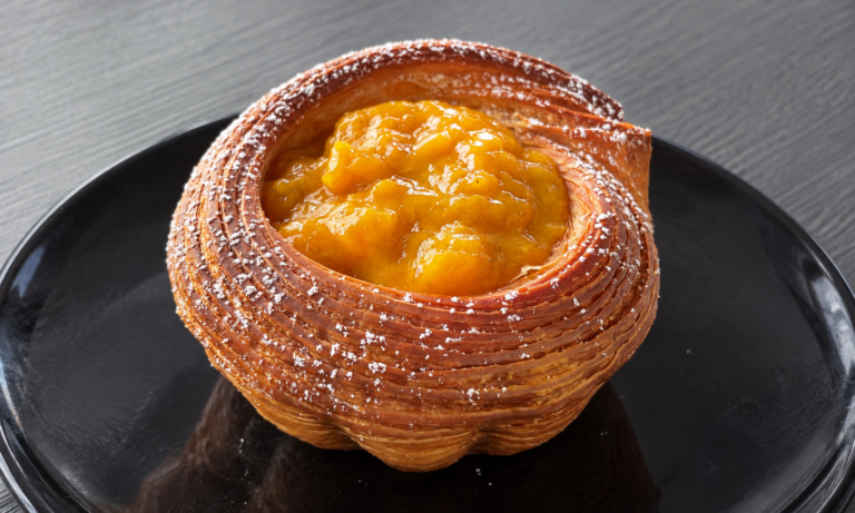 Pain Suisse a cestino con farcitura alla nocciola e mango, zucchero a velo sui bordi e piatto nero.