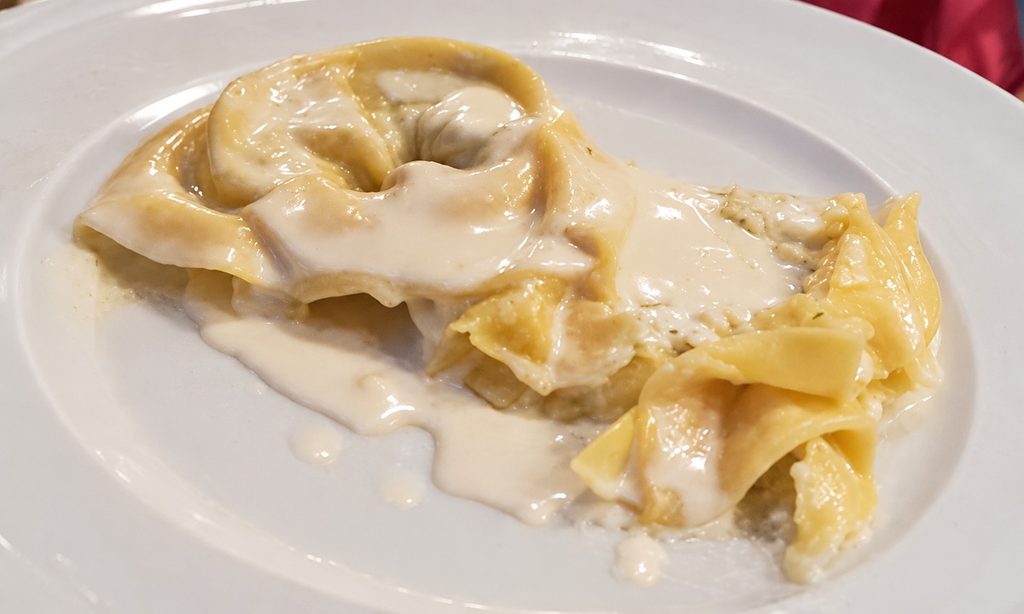 Tortelloni ricoperti di crema di Parmigiano su un piatto bianco.