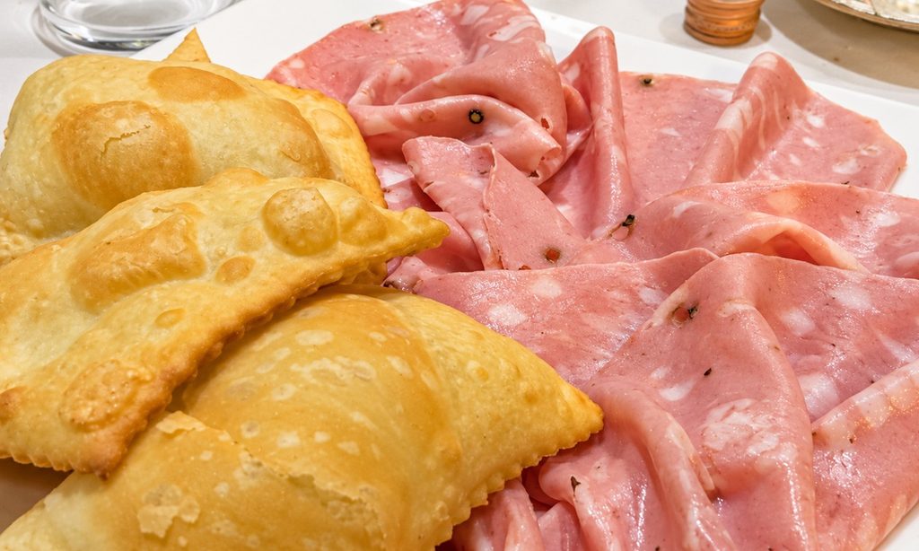 Gnocco fritto dorato e fette di mortadella serviti insieme su un piatto bianco