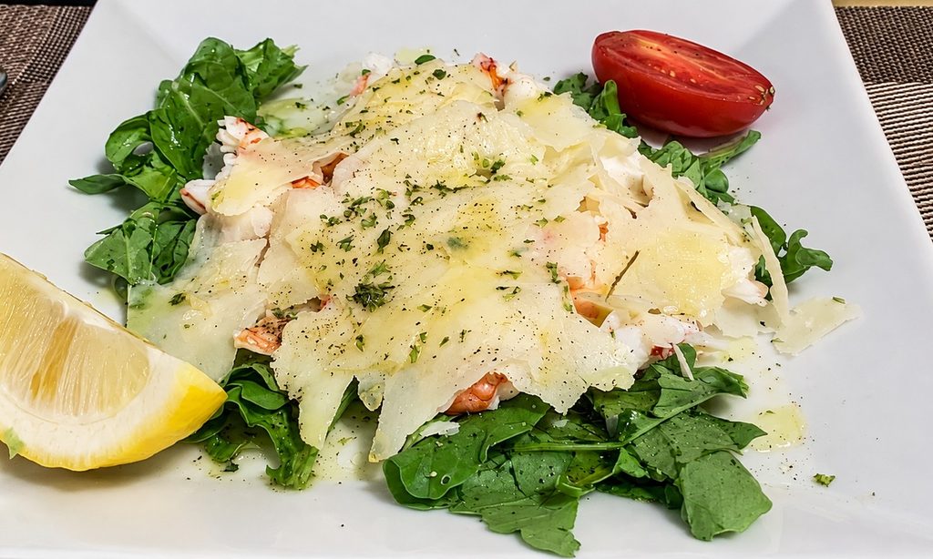 Gamberi su un letto di rucola, coperti da scaglie di Parmigiano, con limone e pomodoro.