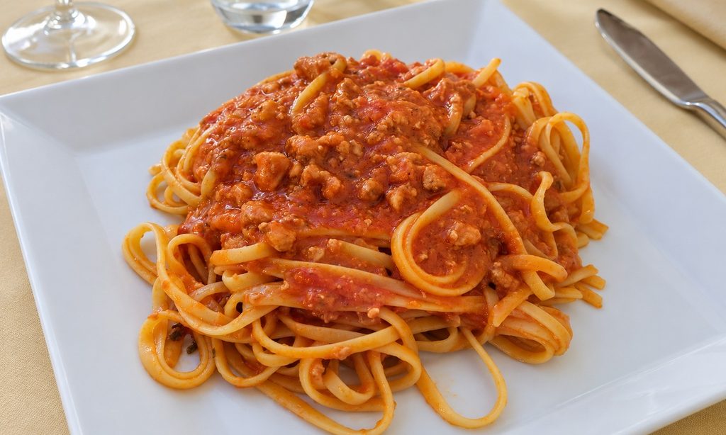 Linguine condite con sugo rosso e pezzetti di pesce spada su un piatto bianco.