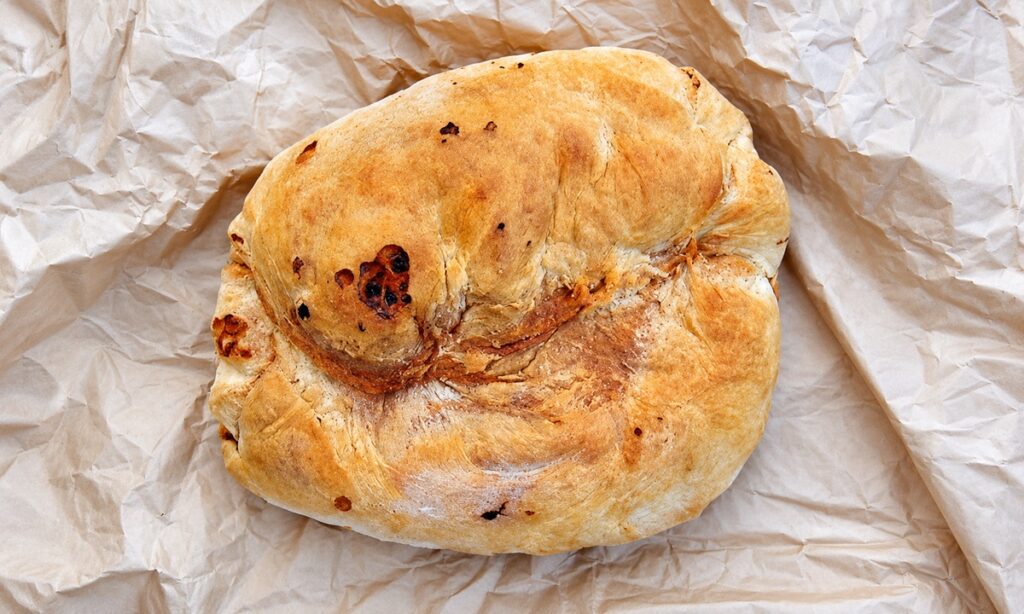 Pagnotta di pane di Cerchiara dalla crosta dorata e dalla forma irregolare, appoggiata sulla carta da forno.
